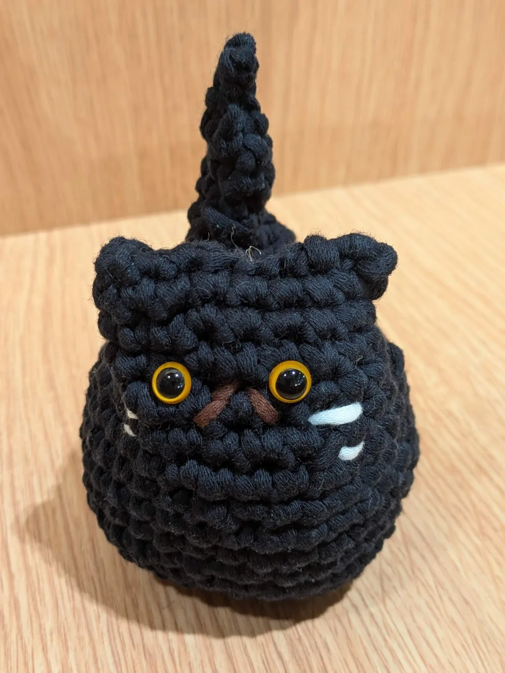 A small crocheted black cat with amber eyes and white whiskers